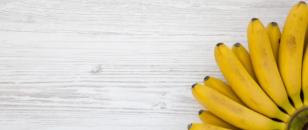 Ramo de plátano bebé en una mesa de madera blanca, vista superior. Puesta plana — Foto de Stock