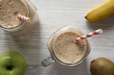 Beyaz w üzerinde muz, kivi, elma smoothie ile dolu cam kavanoz