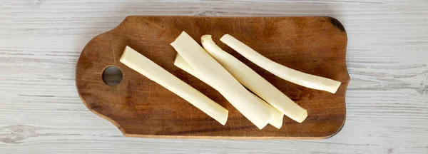 String cheese on rustic wooden board over white wooden backgroun — Stock Photo, Image