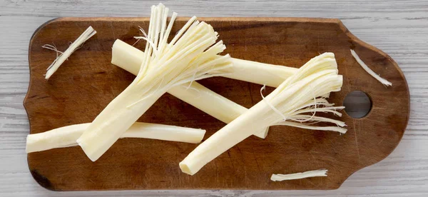 String cheese on rustic wooden board over white wooden surface,