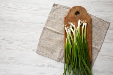 Beyaz ahşap bir masa üzerinde bir kesme tahtası üzerinde taze yeşil soğan, t