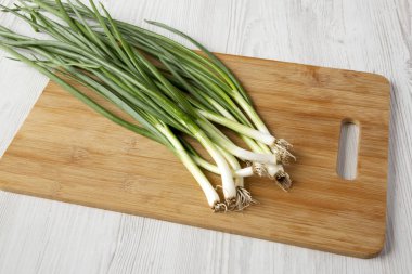 Beyaz ahşap bir yüzey üzerinde bir bambu tahta üzerinde taze yeşil soğan, 