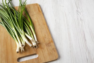 Beyaz ahşap backgroun üzerinde bir bambu tahta üzerinde taze yeşil soğan