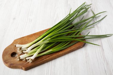 Beyaz ahşap backgrou üzerinde bir kesme tahtası üzerinde taze yeşil soğan