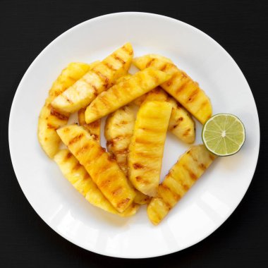 Siyah s üzerinde beyaz bir tabak üzerinde kireç ile ızgara ananas dilimleri