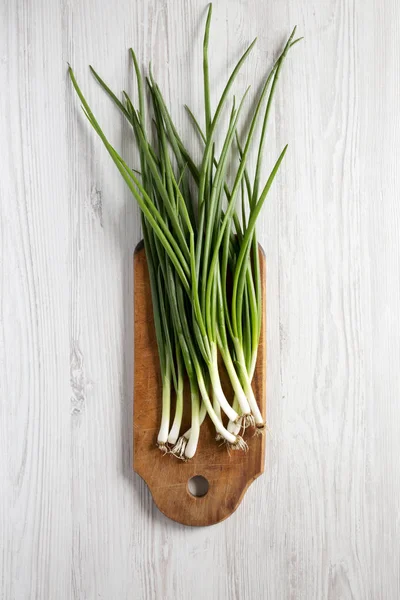 Cebollas verdes frescas en una tabla de cortar sobre un fondo de madera blanca — Foto de Stock