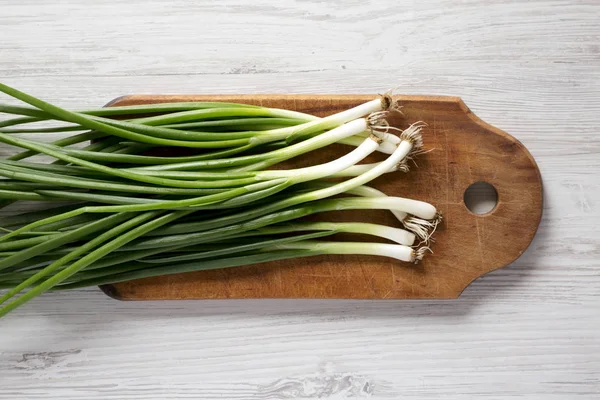 Cebollas verdes frescas en una tabla de cortar sobre una superficie de madera blanca , — Foto de Stock