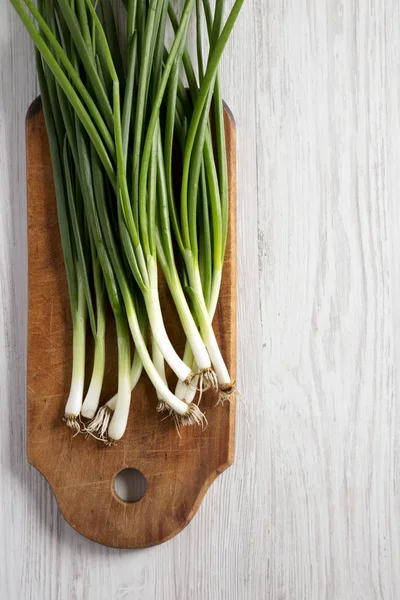 Cebollas verdes frescas en una tabla de cortar sobre una mesa de madera blanca, t — Foto de Stock