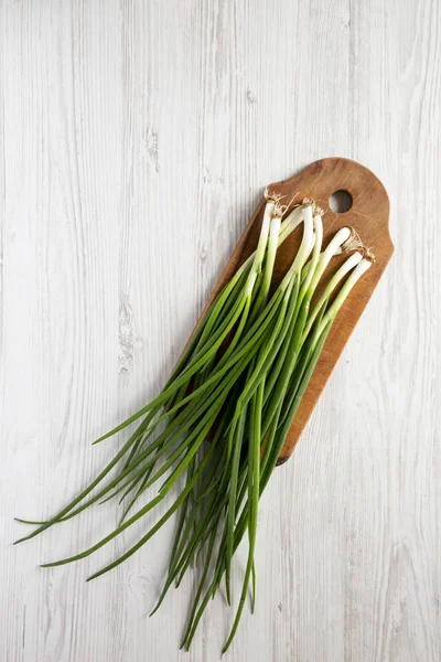 Cebollas verdes frescas en una tabla de cortar sobre un fondo de madera blanca — Foto de Stock