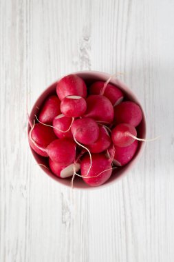 Beyaz ahşap arka plan üzerinde pembe bir kapta taze kırmızı turp, 