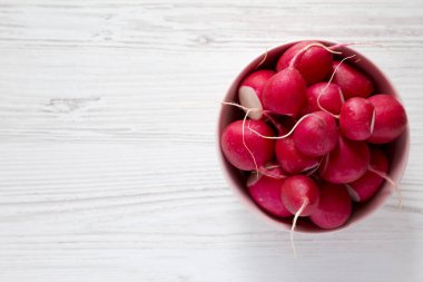 Beyaz ahşap yüzey üzerinde pembe bir kapta taze kırmızı turp, üst