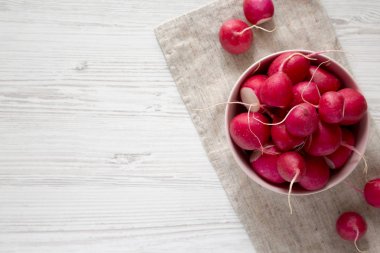 Beyaz ahşap yüzey üzerinde pembe bir kapta taze kırmızı turp, üst