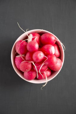 Siyah yüzey üzerinde pembe bir kapta taze kırmızı turp, üst görünümü. 