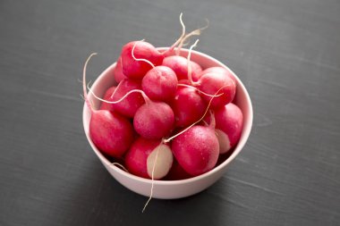 Siyah arka plan üzerinde pembe bir kapta taze kırmızı turp, düşük ang