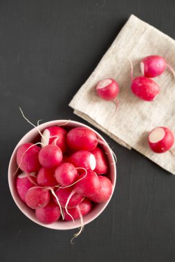 Siyah arka plan üzerinde pembe bir kapta taze kırmızı turp, üst vie