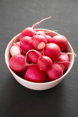 Siyah arka plan üzerinde pembe bir kapta taze kırmızı turp, düşük ang