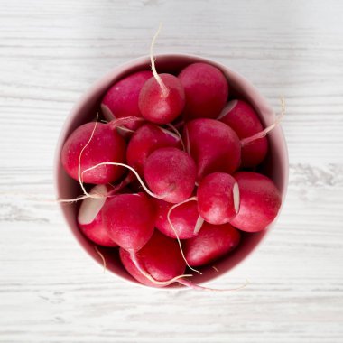 Beyaz ahşap yüzey üzerinde pembe bir kapta taze kırmızı turp, üst