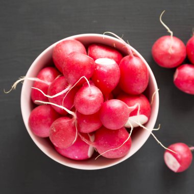 Siyah yüzey üzerinde pembe bir kapta taze kırmızı turp, üst görünümü. 