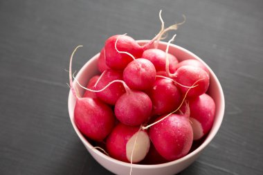 Siyah arka plan üzerinde pembe bir kapta taze kırmızı turp, yan vi