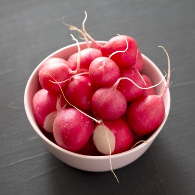 Siyah yüzey üzerinde pembe bir kapta taze kırmızı turp, düşük açı 