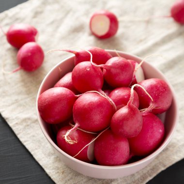 Siyah arka plan üzerinde pembe bir kapta taze kırmızı turp, düşük ang