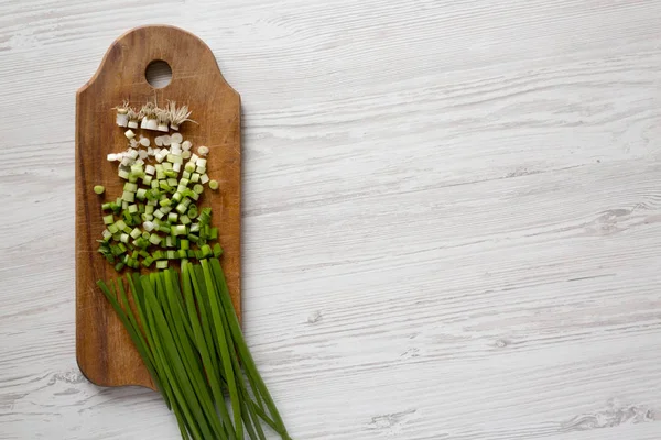 Cebollas verdes picadas en un tablero rústico de madera sobre madera blanca — Foto de Stock