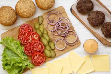 Beyaz ahşap arka planda cheeseburger malzemeler, üst görünüm.
