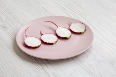 Beyaz ahşap arka plan üzerinde pembe bir tabak üzerinde turp dilimleri, yan