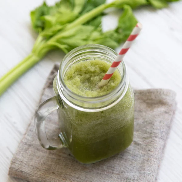 Glass jar of green celery smoothie on a white wooden surface, lo — Stock Photo, Image