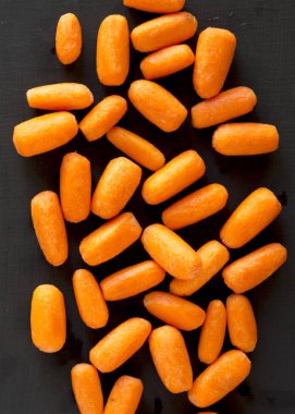 Fresh baby carrots on a black surface, top view. Flat lay, overh clipart