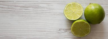 Beyaz ahşap bir yüzey üzerinde yeşil turunçgil limonları var. 
