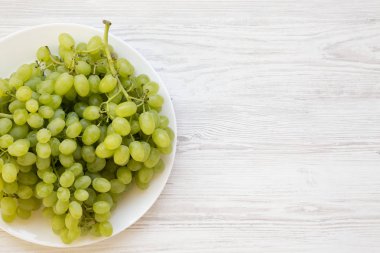 Beyaz ahşap arka plan üzerinde beyaz bir tabak üzerinde yeşil üzüm, üst v