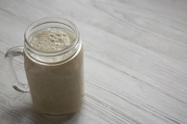 Batido de banana em um frasco de vidro sobre a superfície de madeira branca, lado v — Fotografia de Stock