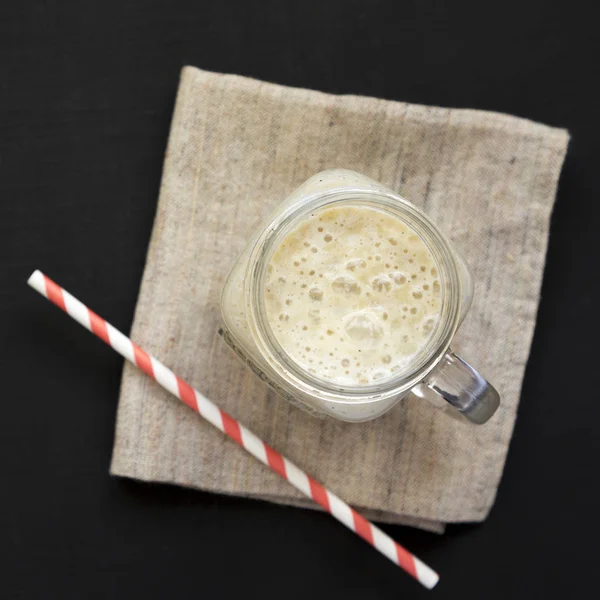 Smoothie de banana em uma caneca de jarra de vidro em uma superfície preta, sobrecarga — Fotografia de Stock