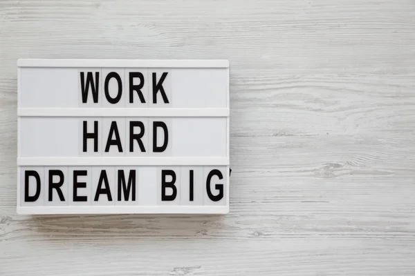 \'Work hard dream big\' words on a lightbox on a white wooden surf