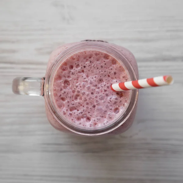 Batido de plátano de fresa en una taza de tarro de vidrio sobre madera blanca — Foto de Stock