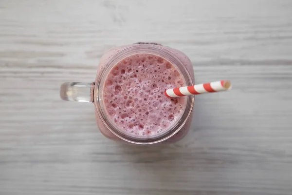 Batido de plátano de fresa en una taza de tarro de vidrio sobre madera blanca — Foto de Stock