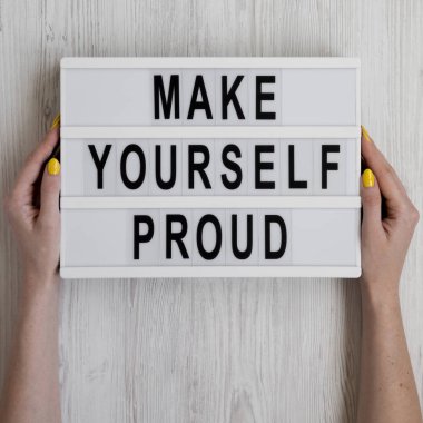 Kadınların elleri 'Kendini gururlandır' sözleriyle aydınlatma kutusunu tutar.