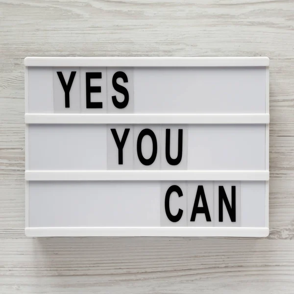 "Yes you can" steht auf einem Leuchtkasten über einer weißen Holzoberfläche. — Stockfoto