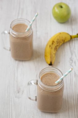 Beyaz ahşap arka plan üzerinde cam kavanozlarda muz elma Smoothie