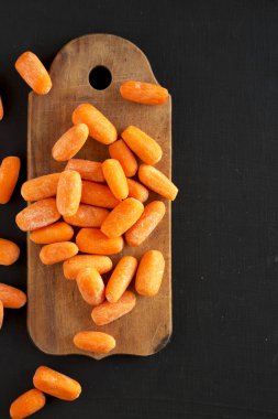 Siyah bir backgrou üzerinde rustik ahşap tahta üzerinde soyulmuş bebek havuç