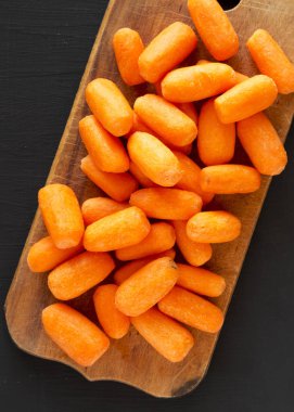 Siyah backgrou üzerinde rustik ahşap tahta üzerinde soyulmuş bebek havuç