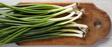 Beyaz ahşap bir yüzey üzerinde bir kesme tahtası üzerinde taze yeşil soğan,