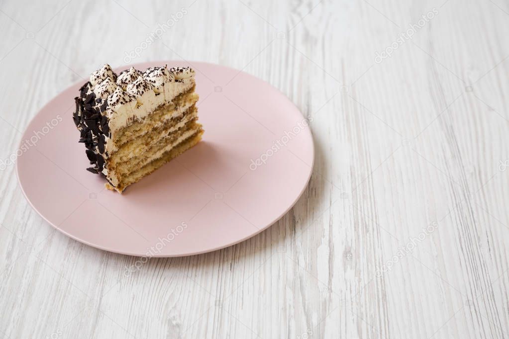 A piece of tiramisu cake on a pink plate on a white wooden backg