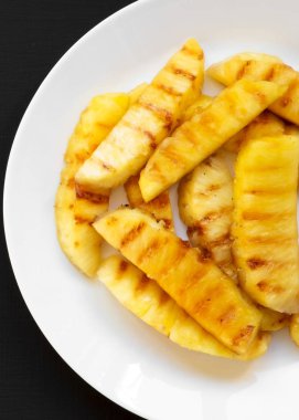 Siyah bir arka plan üzerinde beyaz bir tabak üzerinde Izgara ananas dilimleri.
