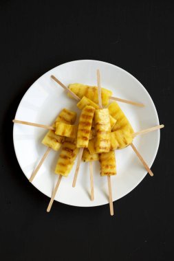 Siyah bir arka plan üzerinde beyaz bir tabak üzerinde Izgara ananas dilimleri,