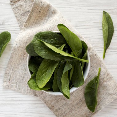 Beyaz ahşap yüzey üzerinde bir kapta çiğ ıspanak, üst görünümü. Overh