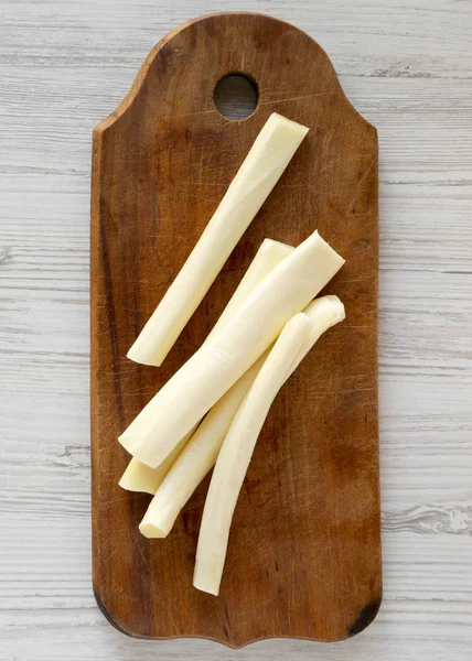 String cheese on a rustic wooden board over white wooden surface — Stock Photo, Image