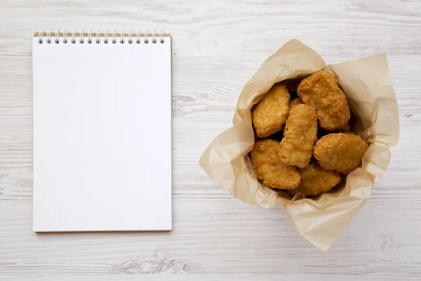 Kip Nuggets in een papieren doos, lege Kladblok over witte houten — Stockfoto