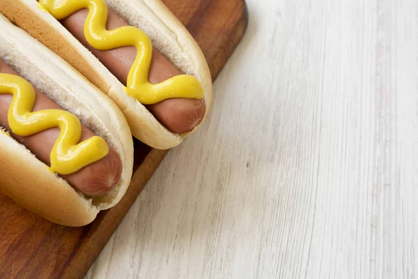 Hotdog med gul sennep på et rustikt træbræt på en hvid m - Stock-foto